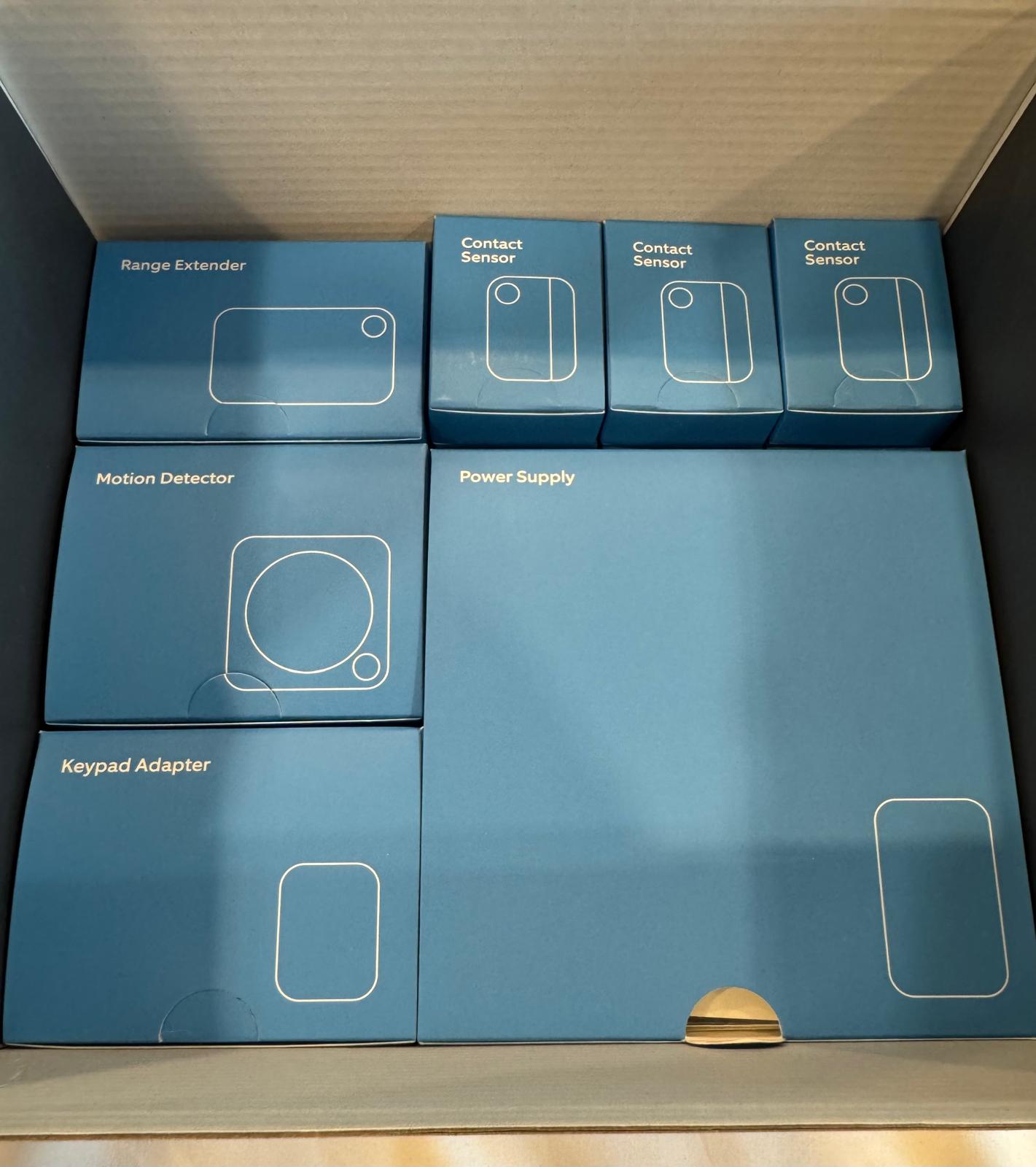 Set of blue boxes labeled with different home security components on a wooden shelf.